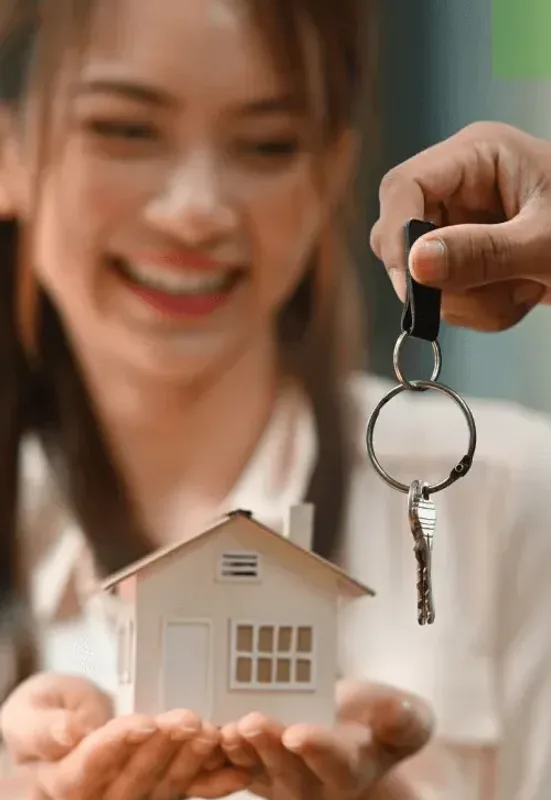 A smiling woman receiving keys while holding a model house
